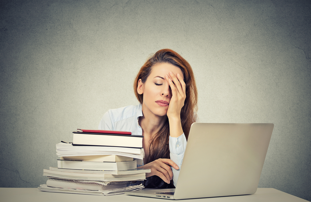 exhausted woman sitting at desk with laptop and books